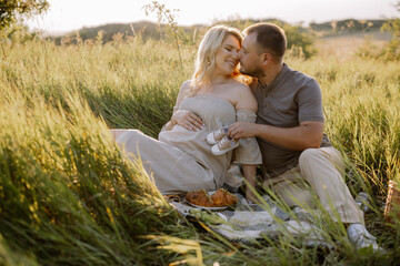 Happy pregnant couple spending time together on a picnic sitting outdoors at sunset in anticipation of a baby boy holding a shoe near the woman's belly.