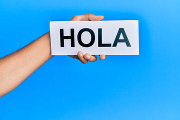Hand of caucasian man holding paper with hola word over isolated blue background © Krakenimages.com