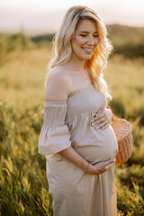 Fototapeta na wymiar Beautiful young blonde pregnant woman holding a straw basket and a bouquet of sunflowers, spending time in nature at sunset. Concept of happy motherhood.