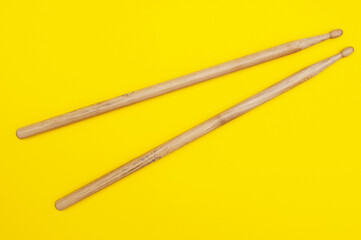 Two wooden drum sticks close up on yellow background