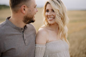 Portrait of a happy pregnant couple with a bouquet of sunflowers spending time together walking in a wheat field at sunset