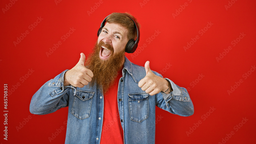 Sticker Young redhead man listening to music doing thumbs up gesture over isolated red background