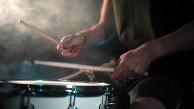 The drummer plays drums in a dark studio with lights on the back.