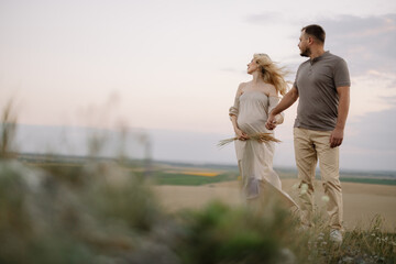 Portrait of a happy pregnant couple with a bouquet of sunflowers spending time together walking in...