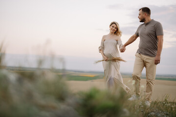 Portrait of a happy pregnant couple with a bouquet of sunflowers spending time together walking in the mountains at sunset