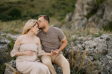 Portrait of a happy pregnant couple with a bouquet of sunflowers spending time together walking in the mountains at sunset