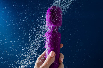 A woman washes a purple vibrator under the shower. Waterproof sex toy on a blue background.