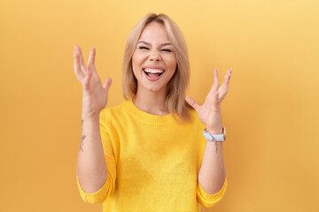 Young caucasian woman wearing yellow sweater crazy and mad shouting and yelling with aggressive...