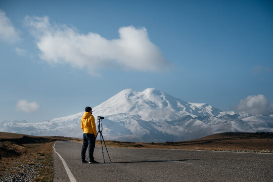 A photographer stands on the road and takes pictures of Elbrus