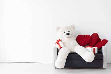 Toy bear with gifts in white room interior with sofa