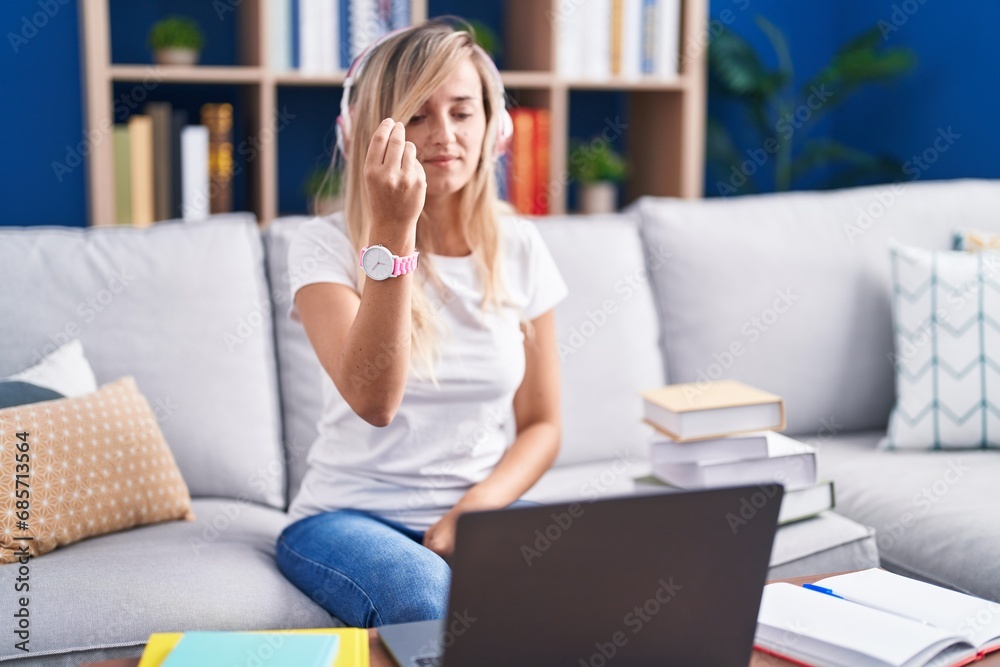 Wall mural young blonde woman studying using computer laptop at home doing italian gesture with hand and finger