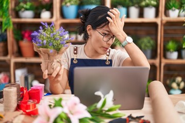 Young hispanic woman working at florist shop doing video call surprised with hand on head for mistake, remember error. forgot, bad memory concept.