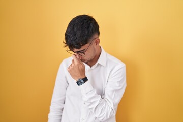 Young hispanic man standing over yellow background tired rubbing nose and eyes feeling fatigue and headache. stress and frustration concept.