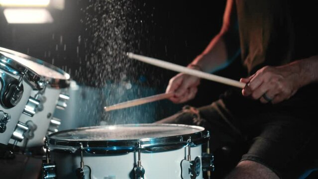 The drummer plays drums in a dark studio with lights on the back.