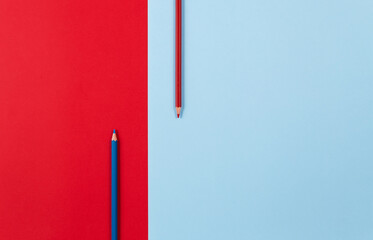 Two pencils blue and red on red- blue paper background. Top view.