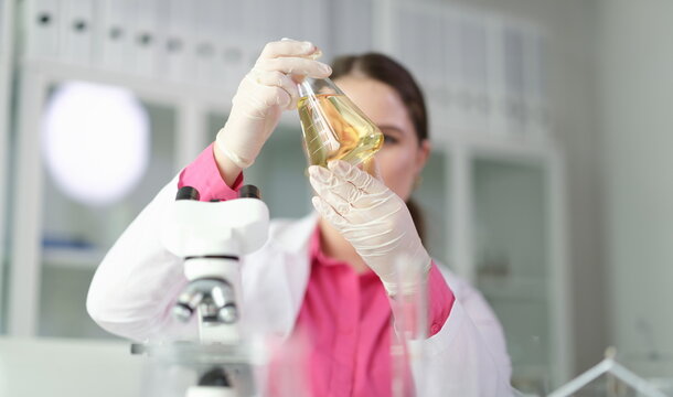 Scientist chemist looking at flask with yellow brake oil in chemistry lab closeup. Quality control of petroleum products concept