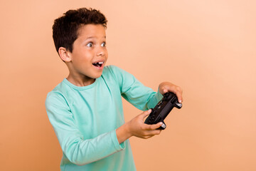 Photo of charming cheerful boy addicted gamer wear stylish clothes have fun playstation empty space isolated on beige color background © deagreez