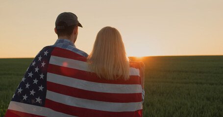 Two farmers with american flag on their shoulders looking forward in wheat field at sunset