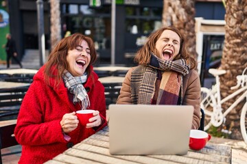 Two women mother and daughter using laptop drinking coffee at coffee shop terrace