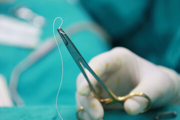Doctor wearing white rubber gloves Hold the suture needle with pliers on the green cloth.