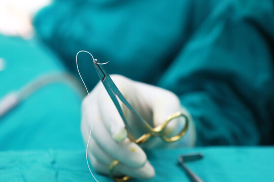 Doctor wearing white rubber gloves Hold the suture needle with pliers on the green cloth.