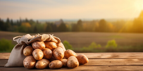 Rustic sack overflowing with potatoes on a wooden table against a hilly, sun-kissed landscape - obrazy, fototapety, plakaty