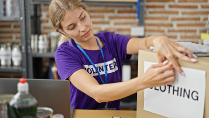 Young blonde woman volunteer packing clothing package to donate at charity center