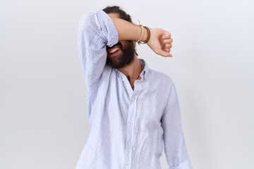 Hispanic man with beard wearing casual shirt covering eyes with arm smiling cheerful and funny. blind concept.