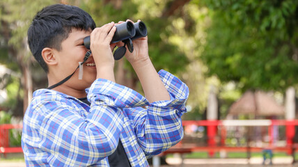 Young Asian boy is using a binocular to lookout for birds and animals in a local park, soft and...
