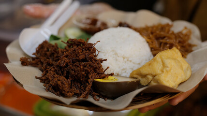 The male trader gives rice, empal meat, chili sauce, orek tempe and vermicelli, making one side dish, nasi empal