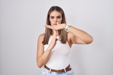 Hispanic young woman standing over white background doing time out gesture with hands, frustrated...