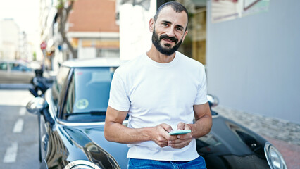 Young hispanic man using smartphone leaning on car at street