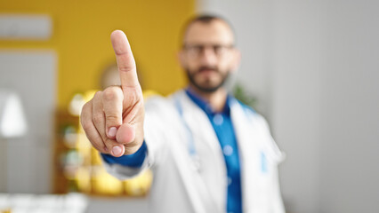 Young hispanic man doctor standing with serious expression saying no with finger at clinic