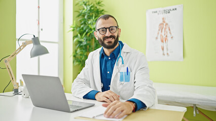 Young hispanic man doctor using laptop working at clinic