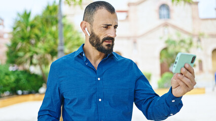 Young hispanic man watching video on smartphone at park