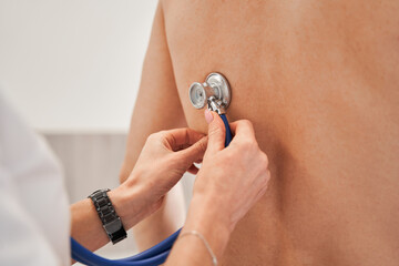 Close up of general practitioner sitting behind the back of patient and using stethoscope