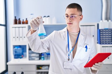 Fototapeta premium Young hispanic man scientist measuring liquid using touchpad at laboratory