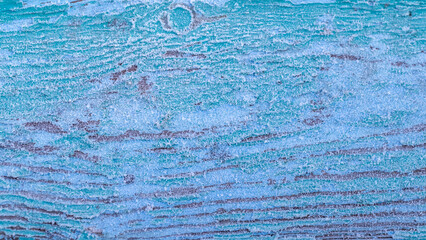 The texture of a board covered with frost, from which the old blue paint lags behind