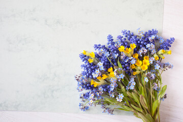 Spring bouquet of blue muscari, forget me not flowers, yellow primrose, paper for  letter text on a decorative background. Greeting card for Mother's Day, Womens Day, Easter, birthday, wedding