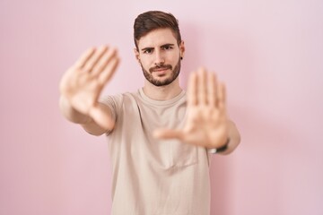 Hispanic man with beard standing over pink background doing frame using hands palms and fingers, camera perspective