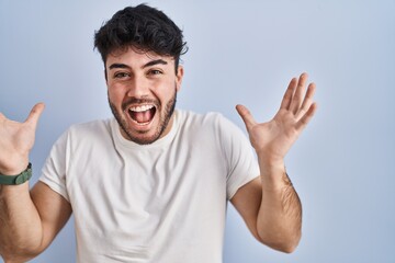 Naklejka premium Hispanic man with beard standing over white background celebrating crazy and amazed for success with arms raised and open eyes screaming excited. winner concept