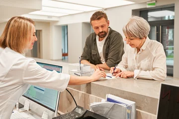 Patients signing agreement and talking to professional receptionist in clinic © Yakobchuk Olena