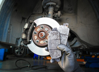 Used car brake pads in the hands of a mechanic with brake discs and brake calipers on the...