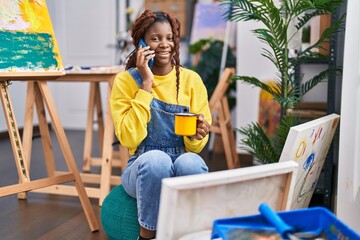 African american woman artist talking on smartphone drinking coffee at art studio