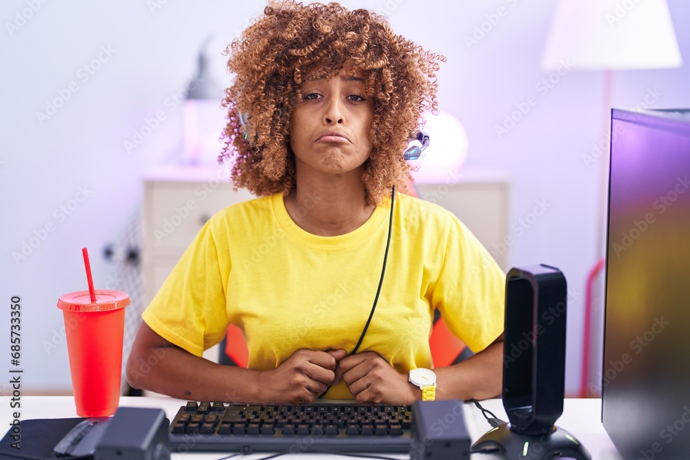 Sticker Young hispanic woman with curly hair playing video games wearing headphones depressed and worry for distress, crying angry and afraid. sad expression.