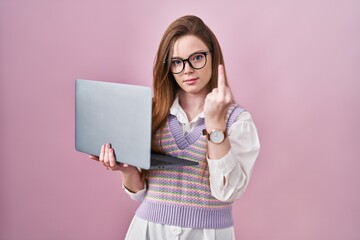 Young caucasian woman working using computer laptop showing middle finger, impolite and rude fuck off expression