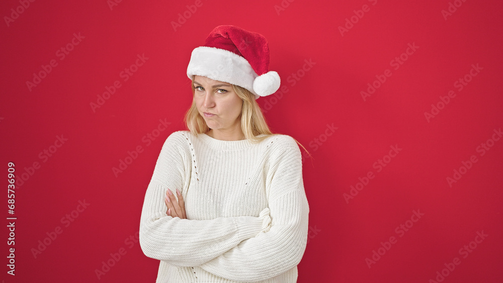 Sticker Young blonde woman standing upset wearing christmas hat over isolated red background