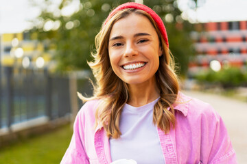 Positive woman in casual red hat and stylish clothes holding coffee cup, looking at camera