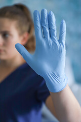 Girl in medical suit holding palm in blue glove showing at camera just place for text hospital