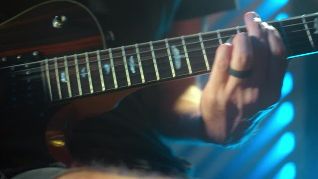 The young musician's hands play electro guitar in a dark studio with a light at the back